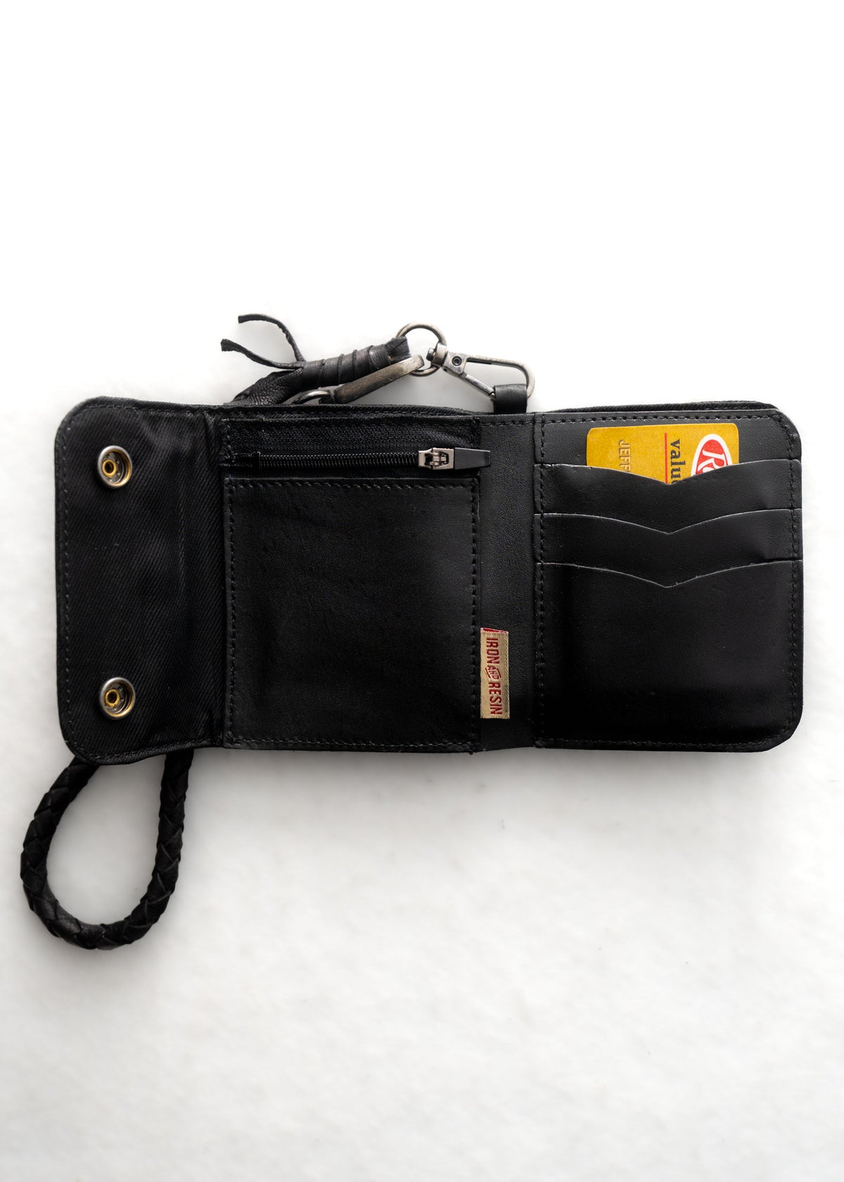 Black leather wallet open, showing card slots, a zippered pocket, and a braided strap on a white background.