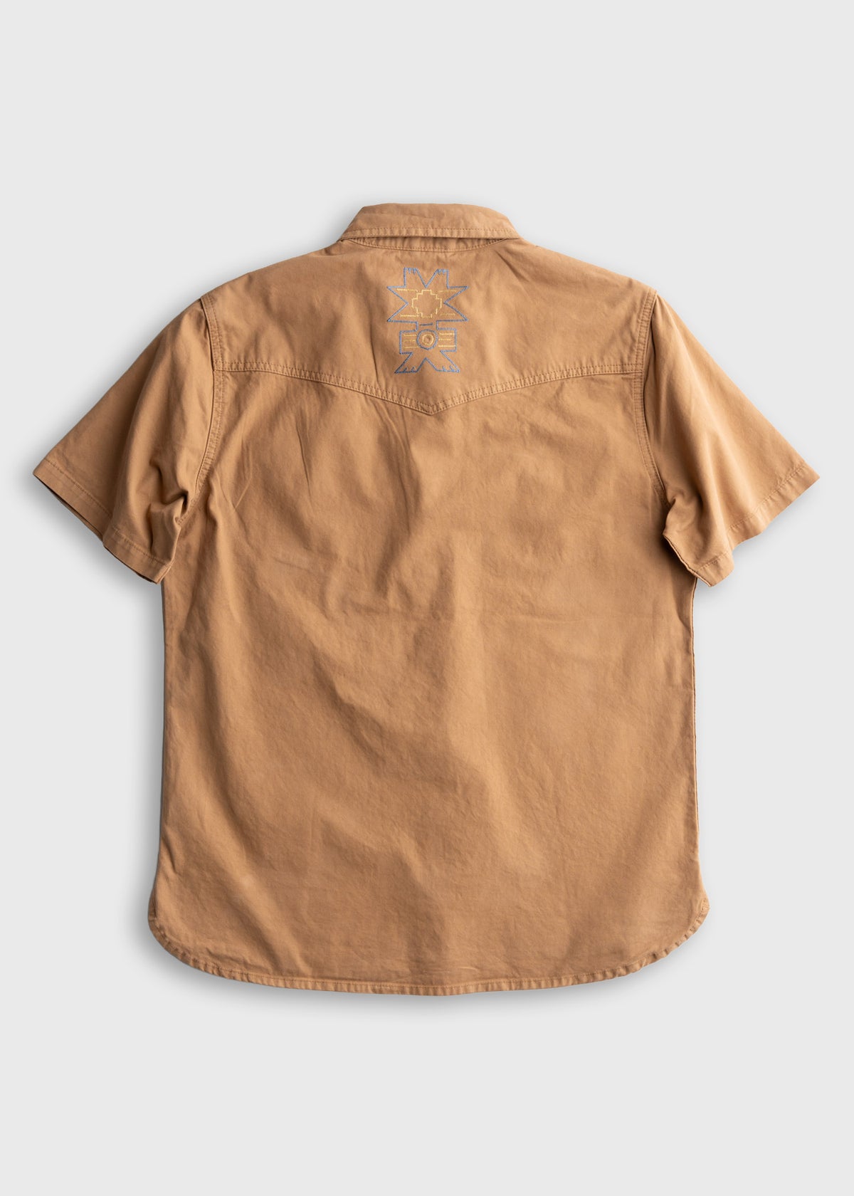 Back view of a tan short-sleeve shirt with a geometric design on the upper back, set against a plain background.