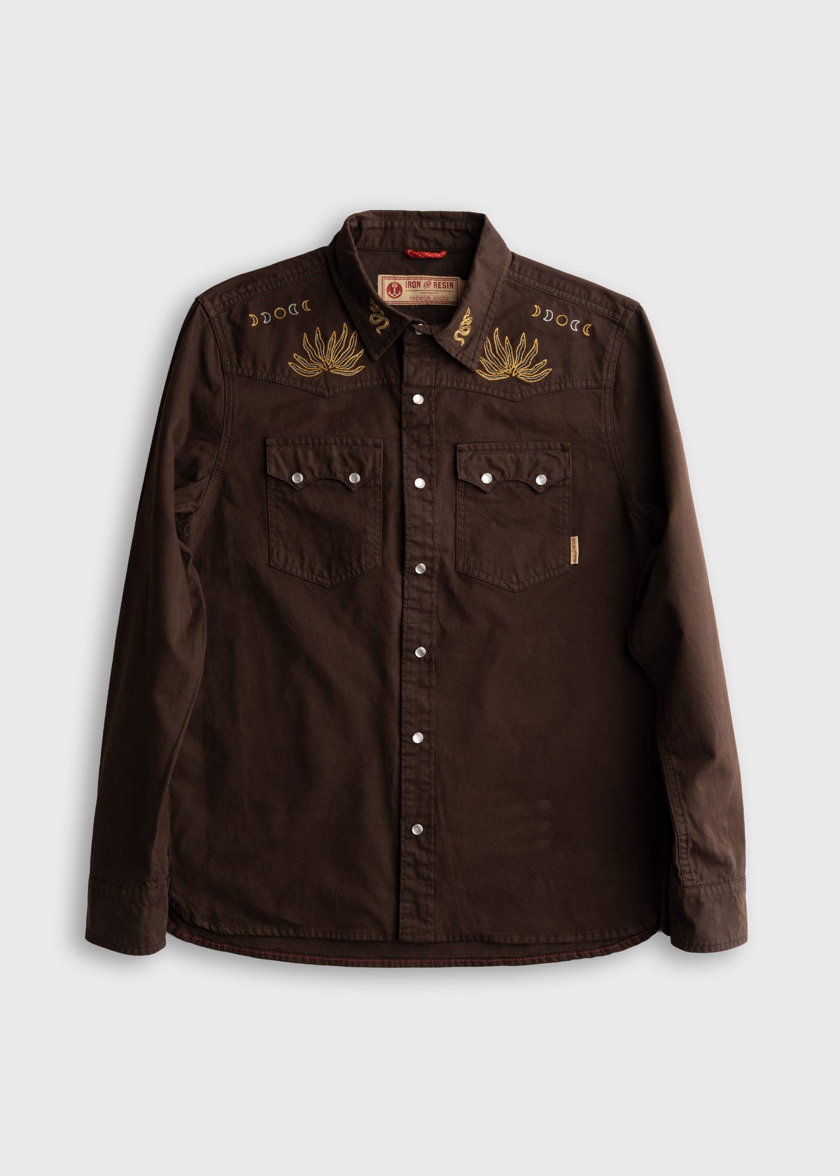 Brown western shirt with gold embroidery on the shoulders, featuring snap buttons and two chest pockets, laid flat on white.