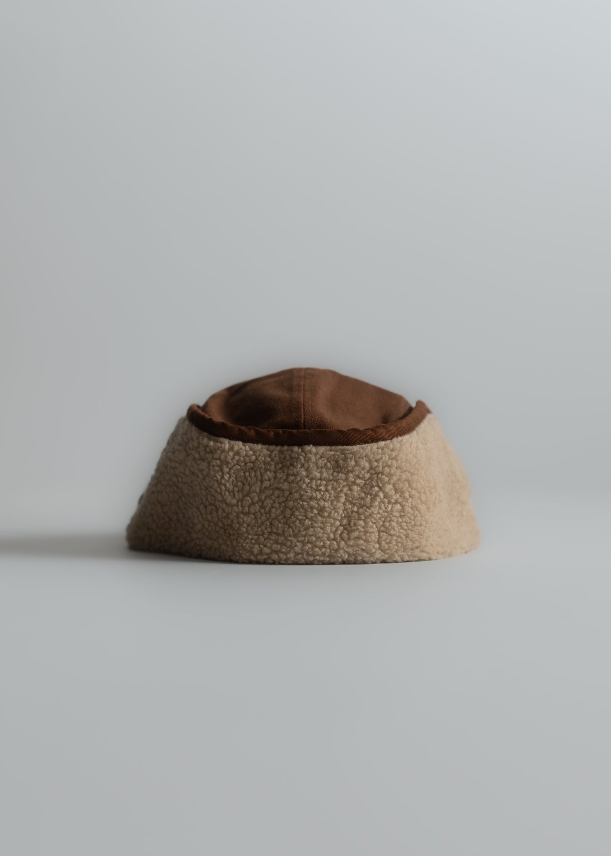 A cozy, brown and beige sherpa bucket hat sits on a plain surface, showcasing its soft texture and simple design.