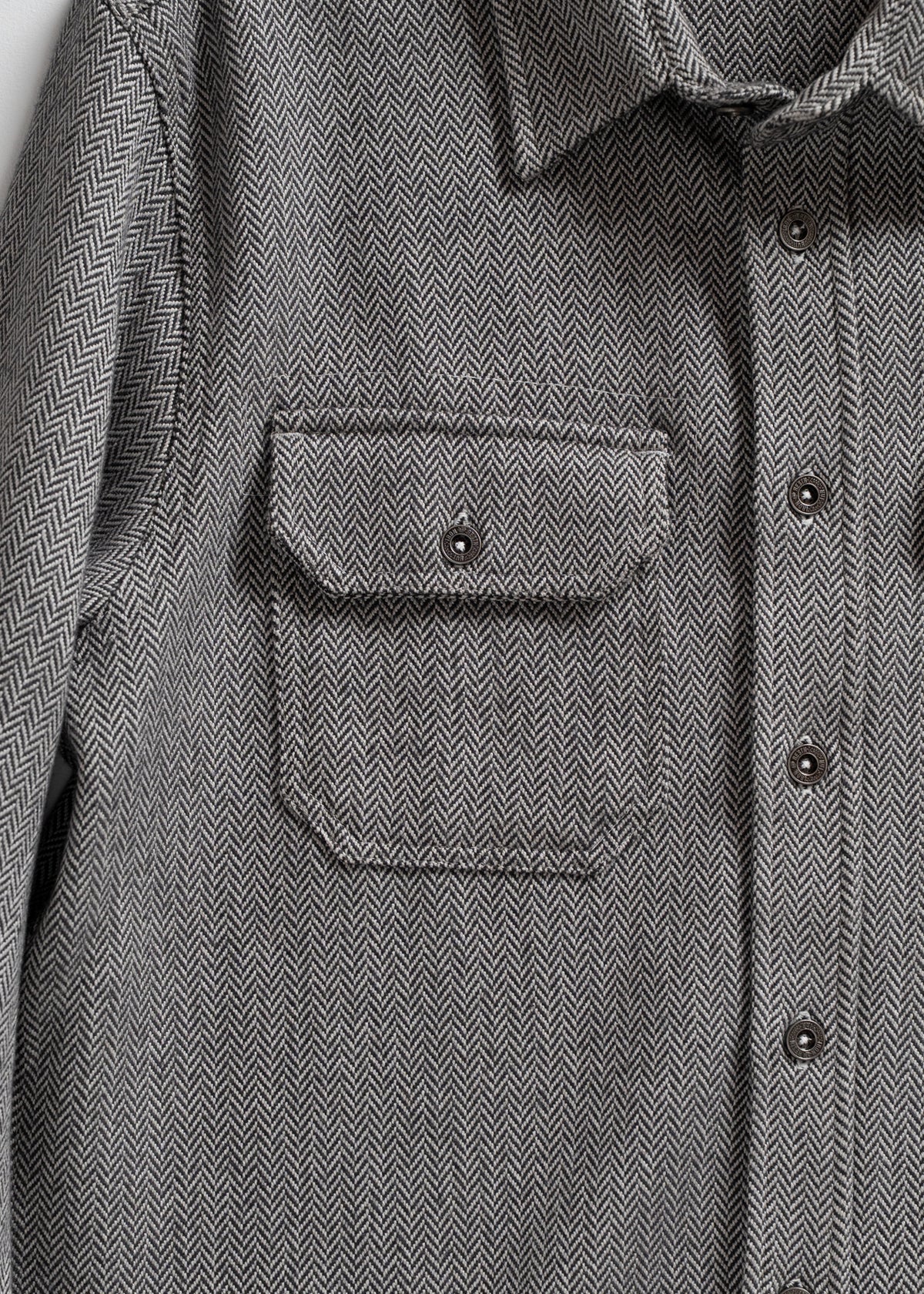 Gray herringbone shirt with buttoned front and chest pocket, showcasing detailed fabric pattern and classic design.