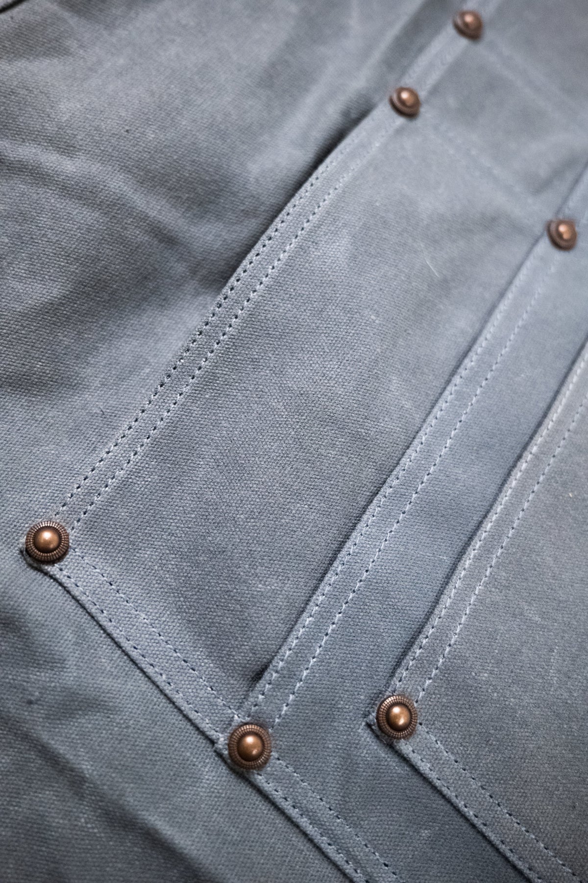 Close-up of blue fabric with visible stitching and metal rivets, showcasing texture and design details.