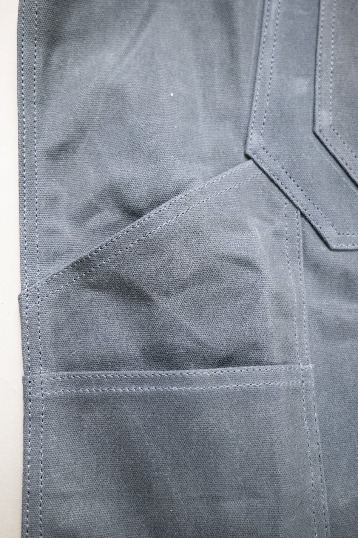 Close-up of a gray fabric apron with visible stitching and pocket detail, showcasing durable material and craftsmanship.