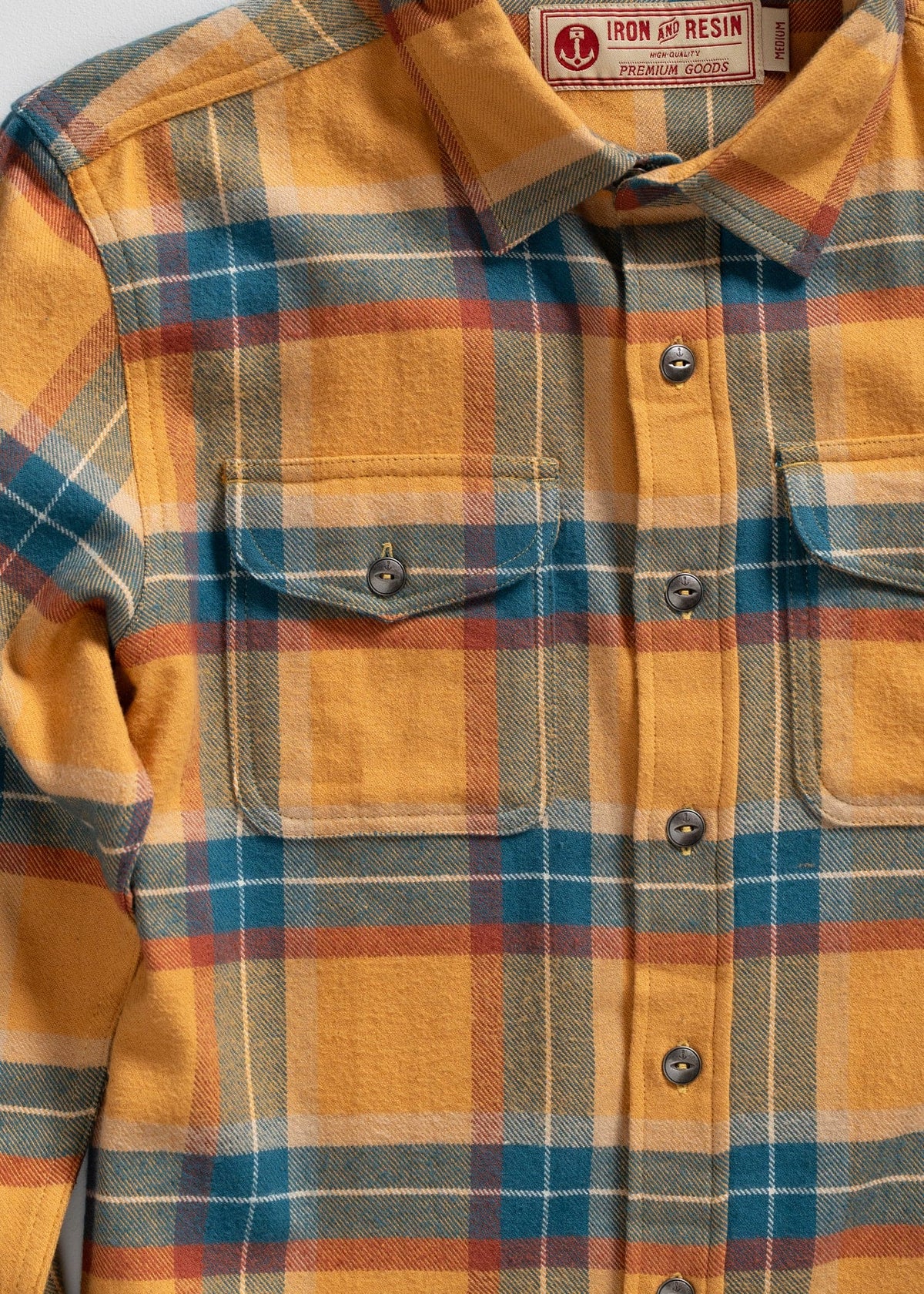 Yellow, blue, and red plaid flannel shirt with buttoned pockets, labeled "Iron and Resin Premium Goods," medium size.