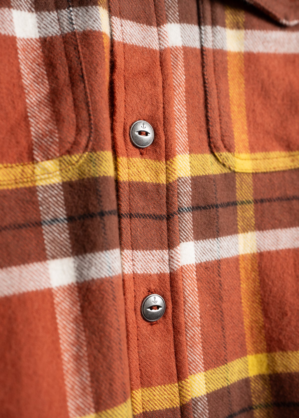 Close-up of a red, yellow, and white plaid flannel shirt with metal buttons, highlighting the fabric's texture and pattern.