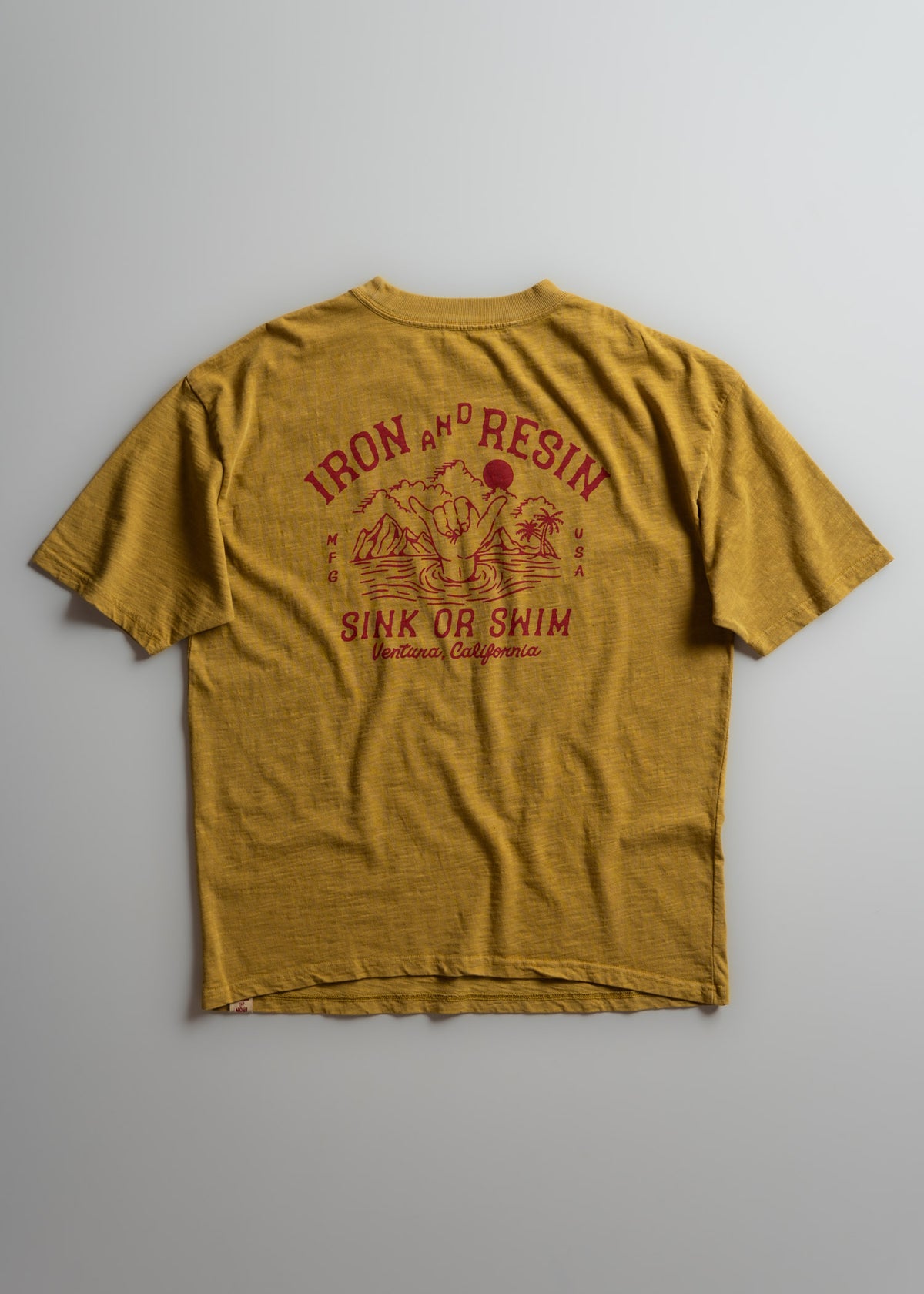 Yellow T-shirt with "Iron and Resin" and "Sink or Swim" in red text, featuring a hand and wave graphic. Ventura, California.