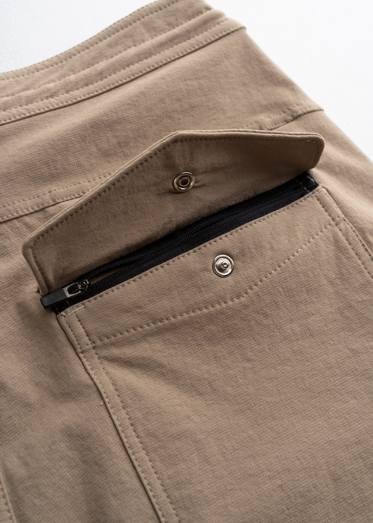 Close-up of khaki pants with a snap button and zipper pocket, showcasing secure storage and durable stitching details.