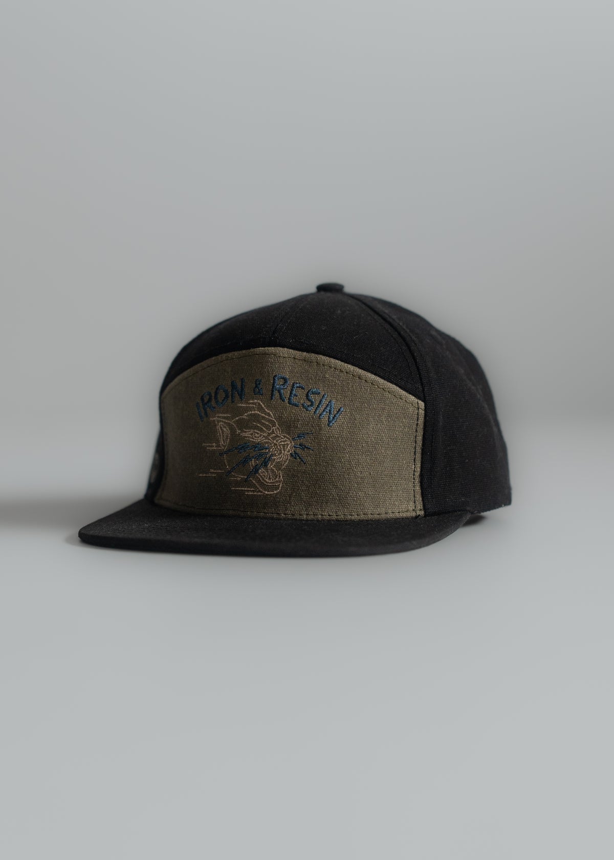 Black cap with "Iron & Resin" logo on olive front panel, featuring a motorcycle design, placed on a plain gray background.