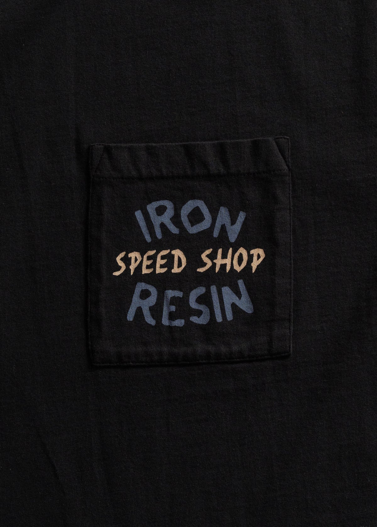 Black shirt pocket with "Iron Resin Speed Shop" text in bold, contrasting colors, creating a vintage, rugged aesthetic.