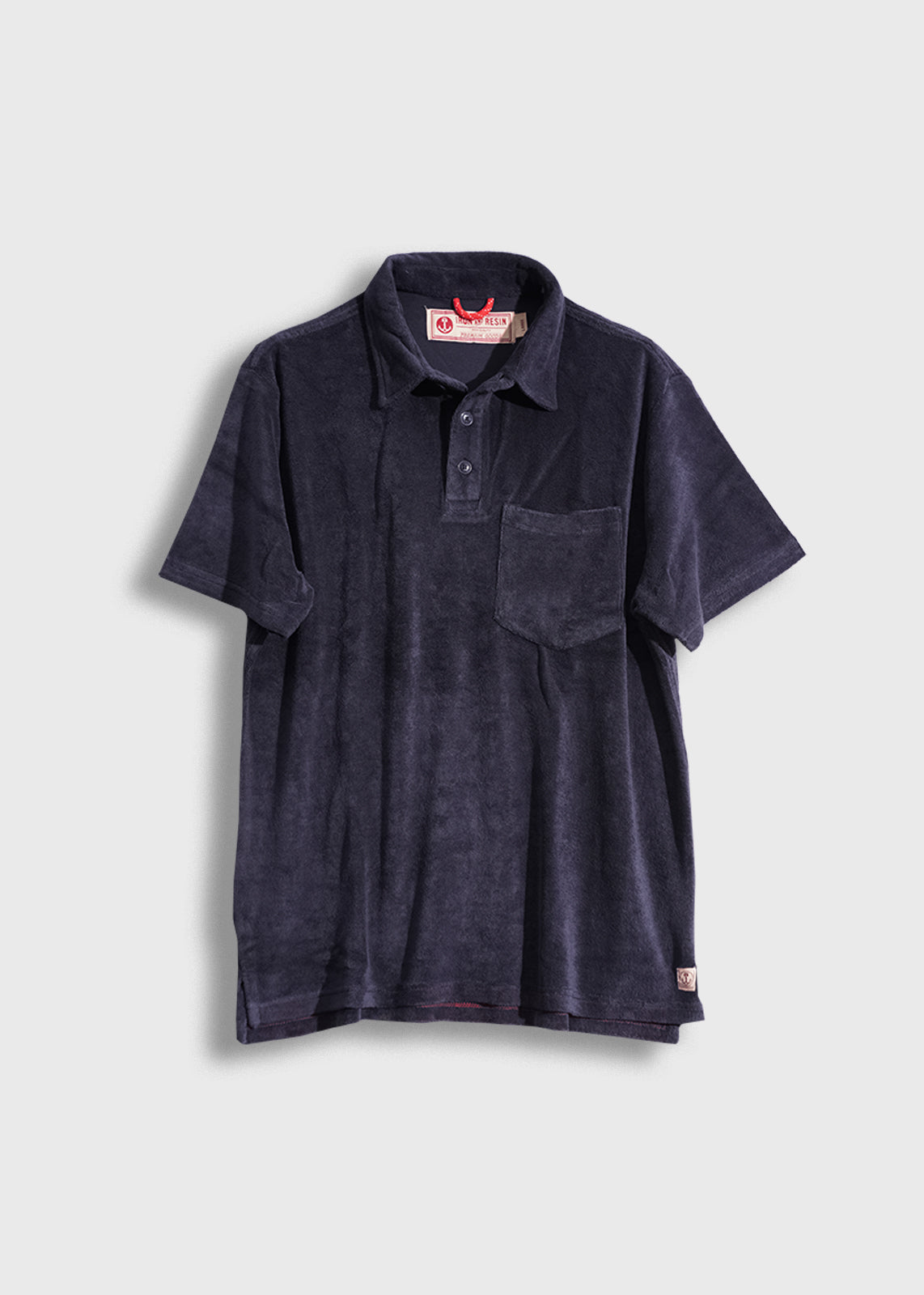Navy blue terry cloth polo shirt with a pocket, buttoned collar, and red label, displayed against a plain background.