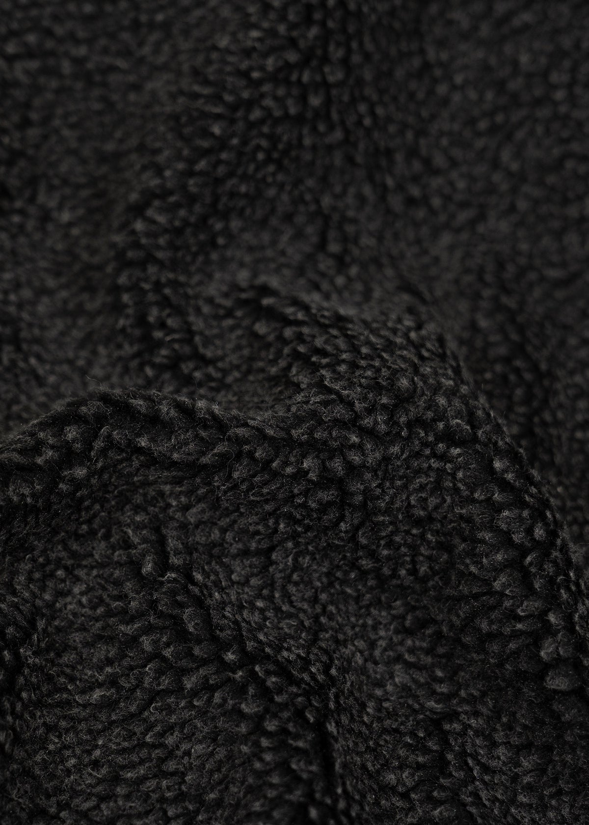 Close-up of black fleece fabric texture, showing soft, curly fibers and a cozy, warm appearance.