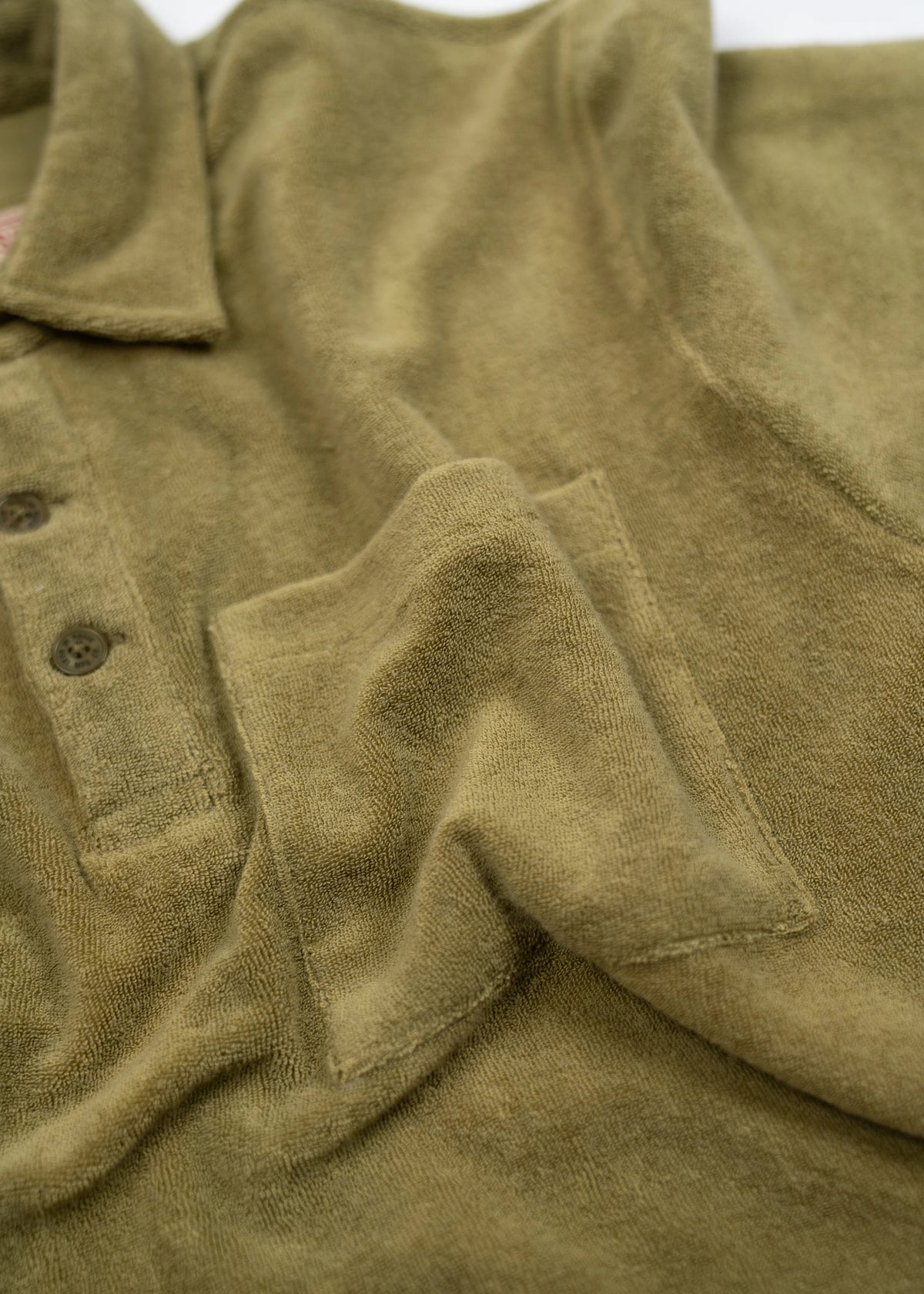 Olive green terry cloth polo shirt with buttons and a pocket, showcasing soft texture and casual style.