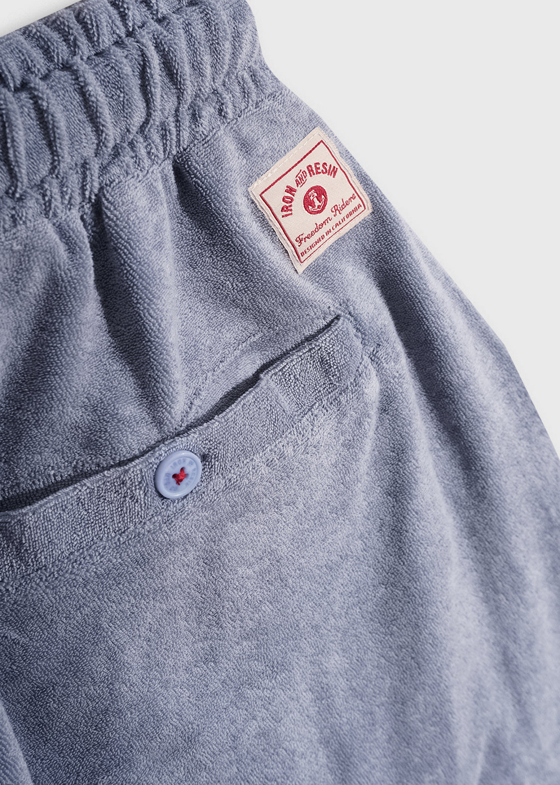 Blue terry cloth shorts with a buttoned back pocket and red "Iron and Resin" label, showcasing casual style and comfort.