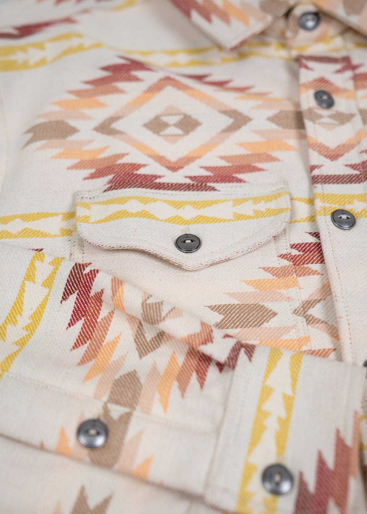 Close-up of a shirt with a geometric pattern in earthy tones, featuring a buttoned pocket and collar detail.