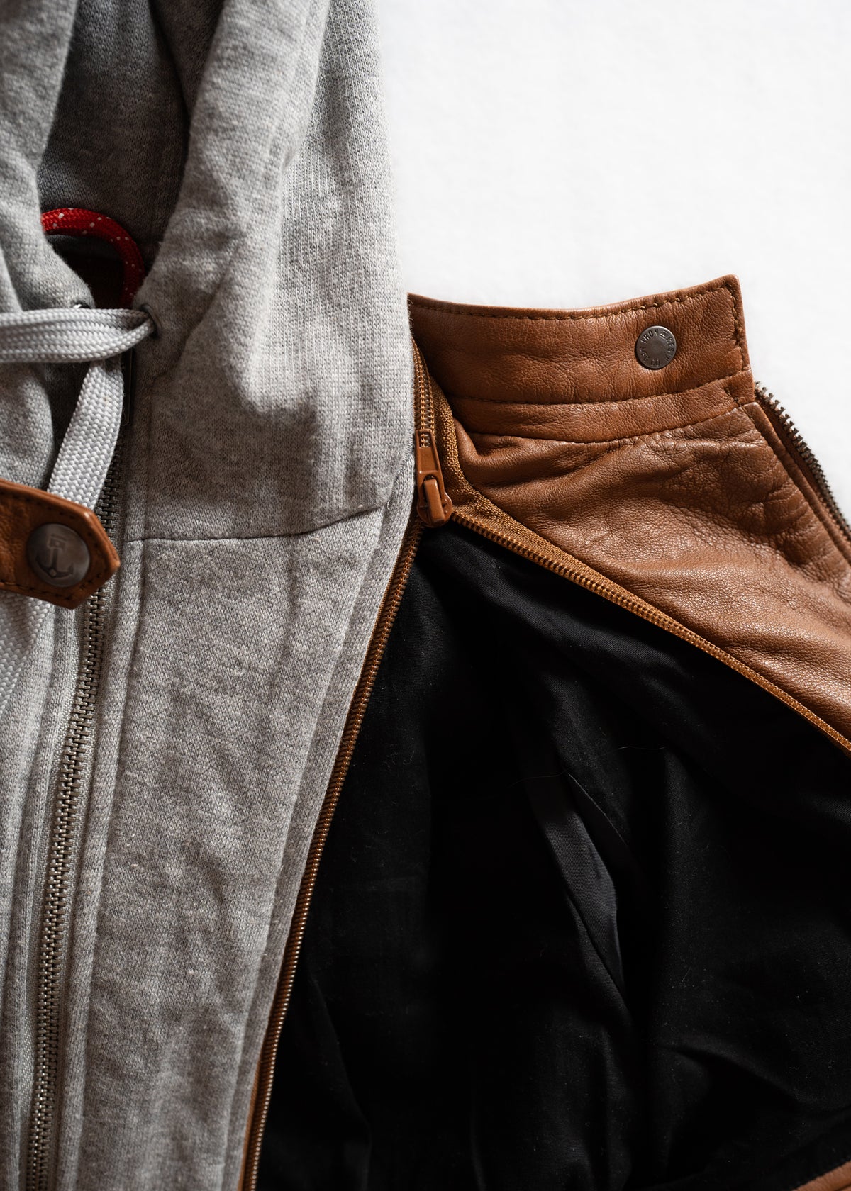 Close-up of a gray hoodie and brown leather jacket side by side, highlighting contrasting textures and colors.
