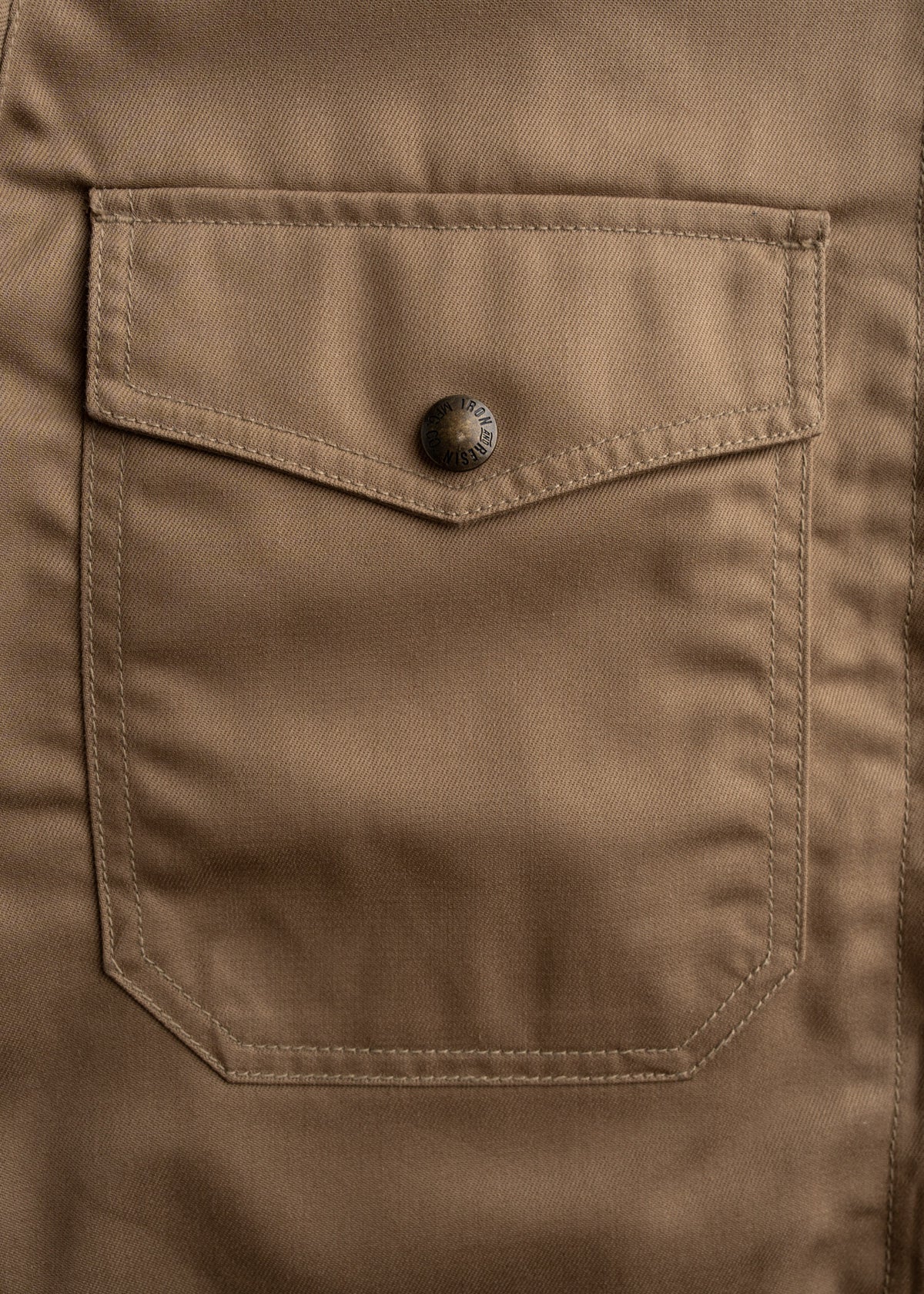 Close-up of a brown fabric pocket with a metal button, showcasing detailed stitching and texture.
