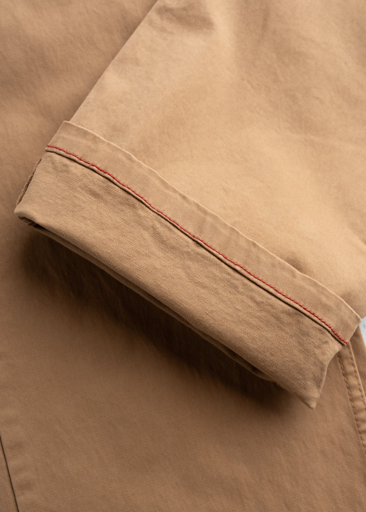 Close-up of a beige pant leg with a rolled cuff and visible red stitching detail, highlighting the fabric texture and craftsmanship.