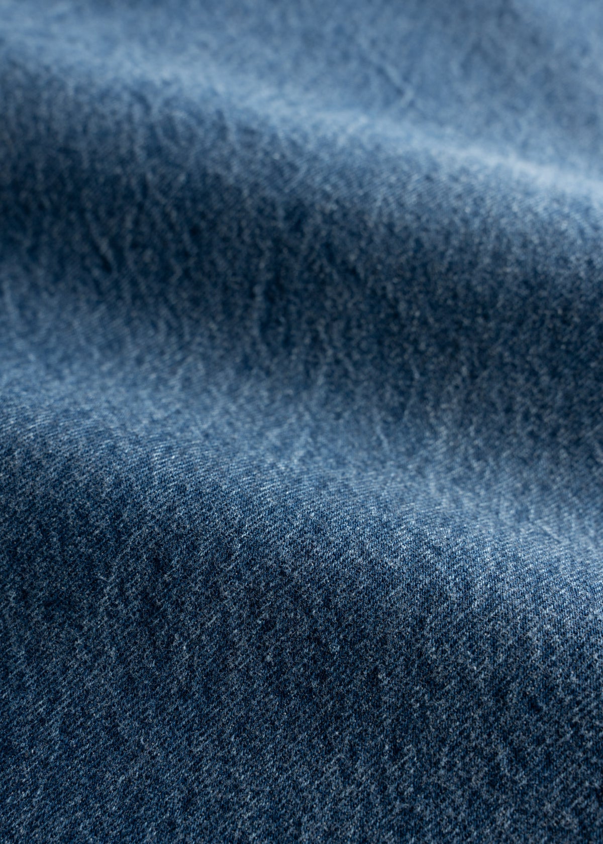 Close-up of blue denim fabric with a textured surface, showing subtle variations in color and weave, creating a wavy pattern.