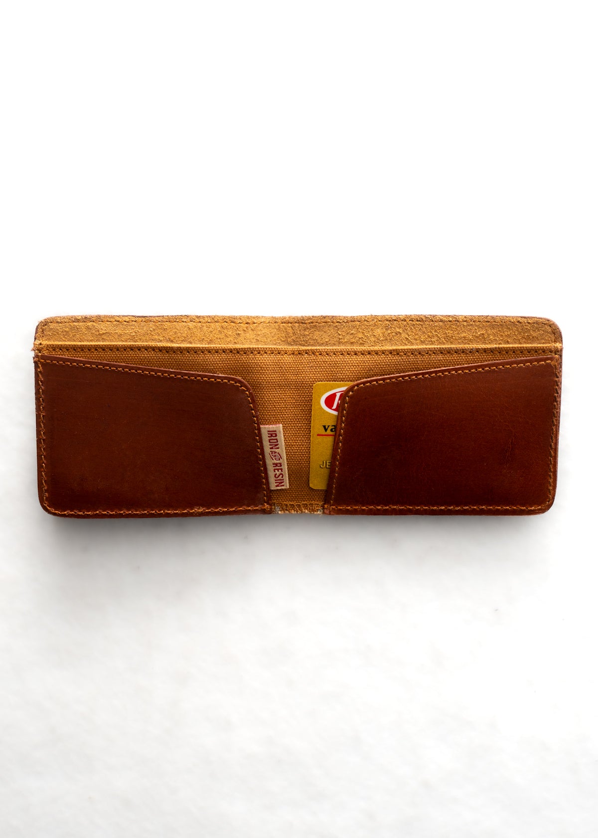 Open brown leather wallet with two visible card slots, holding a yellow card. The wallet is placed on a white background.