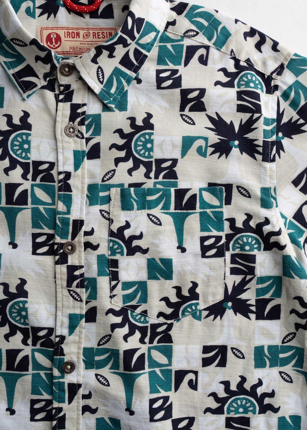 Patterned shirt with abstract shapes in teal and black. Features a front pocket and button-down design. Iron and Resin label visible.