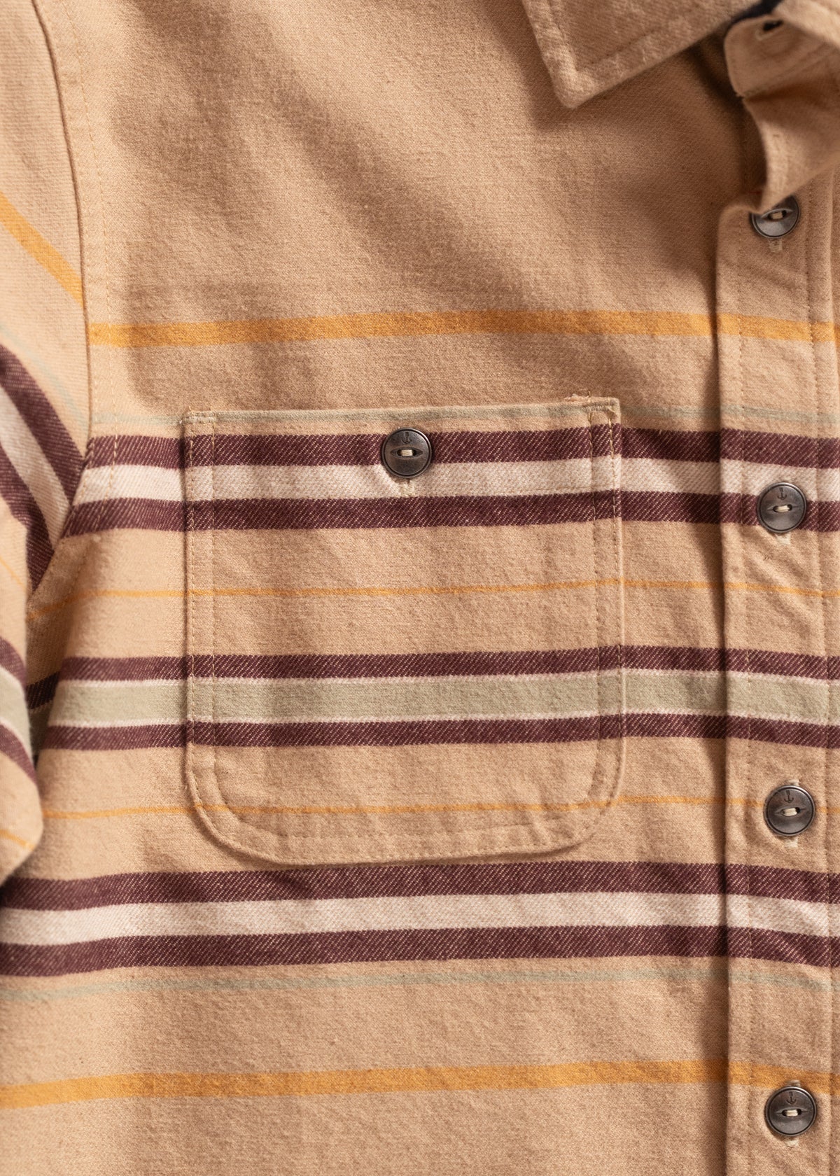 Close-up of a beige flannel shirt with brown and yellow stripes, featuring a buttoned chest pocket and collar detail.