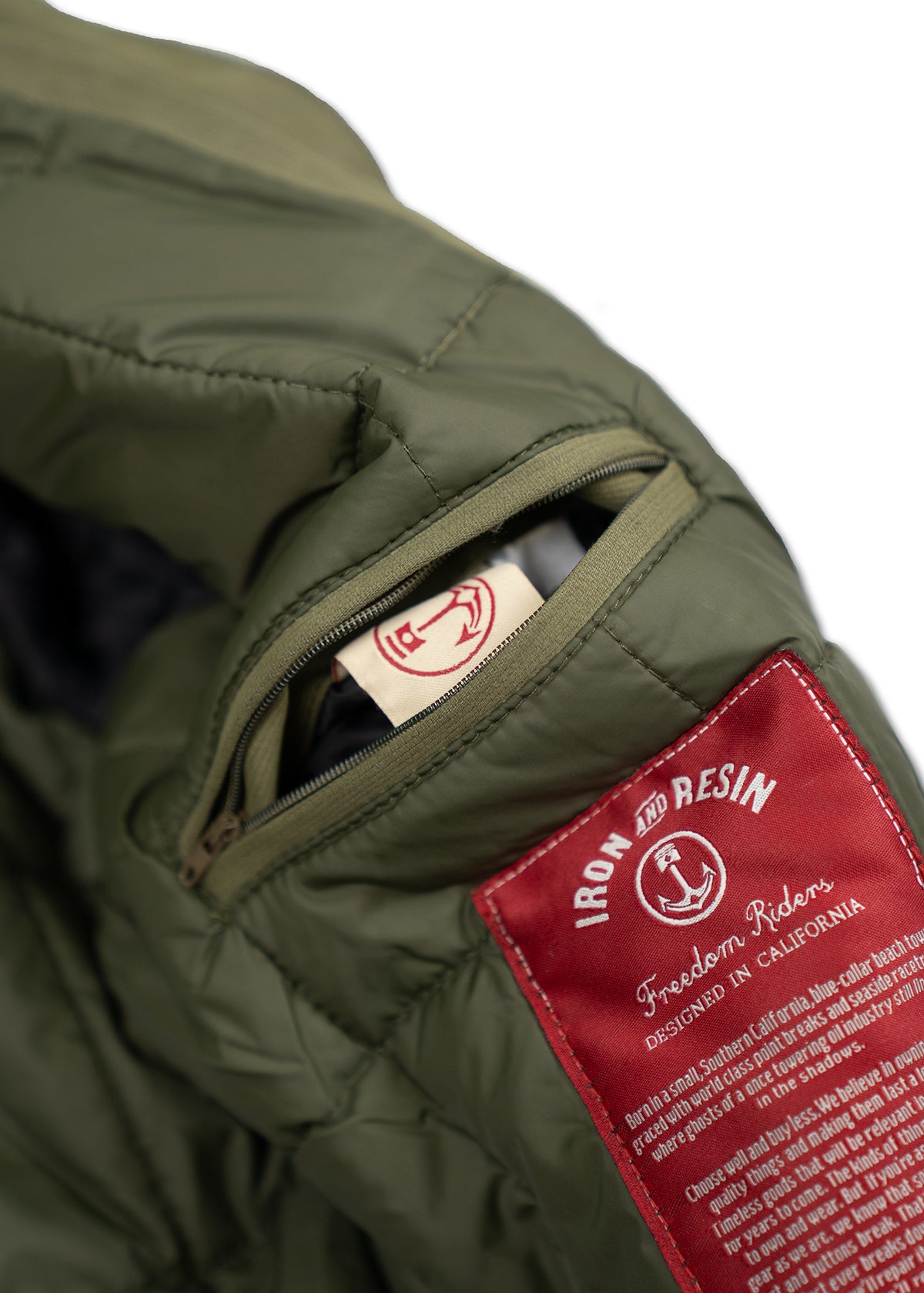 Green jacket with a red Iron and Resin label and an open pocket showing a logo tag. Designed in California.