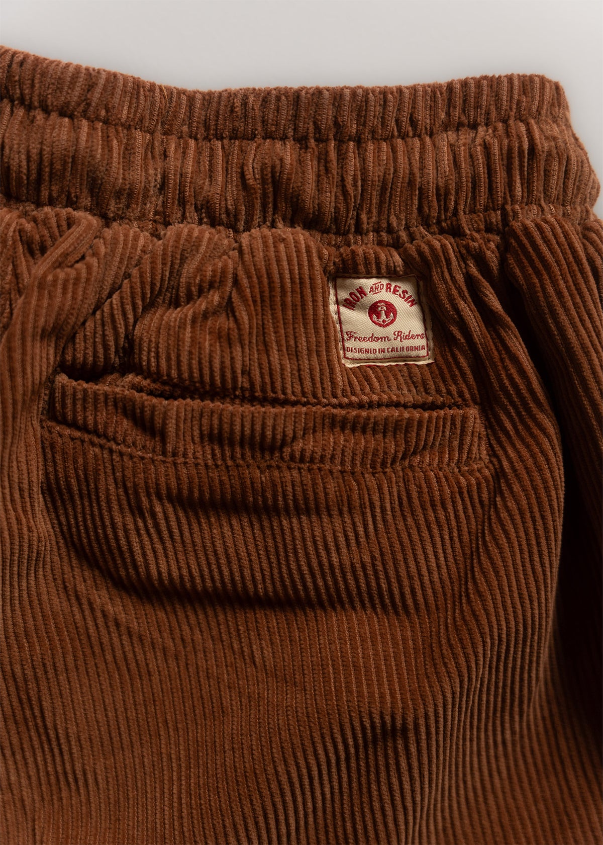 Brown corduroy pants with an elastic waistband and a visible label reading "Iron and Resin, Freedom Riders, Designed in California."