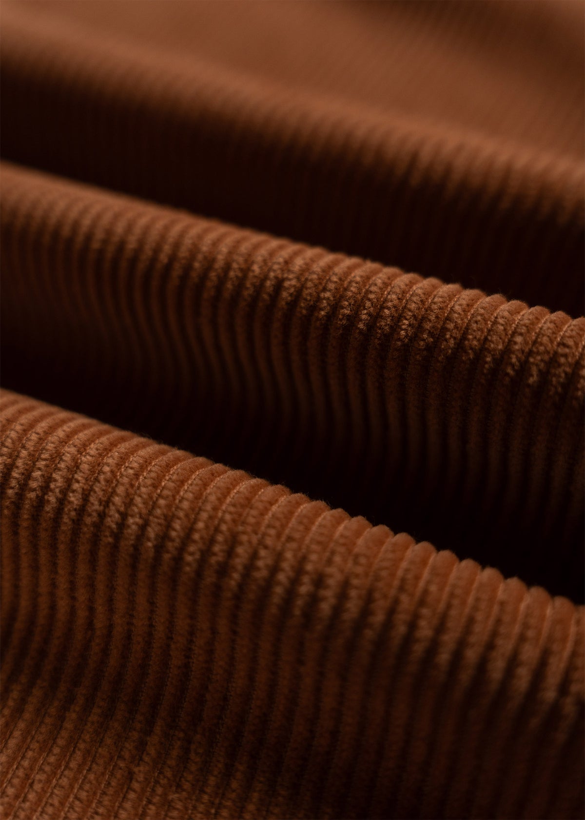Close-up of brown corduroy fabric, showcasing its textured ridges and soft, velvety surface under gentle lighting.