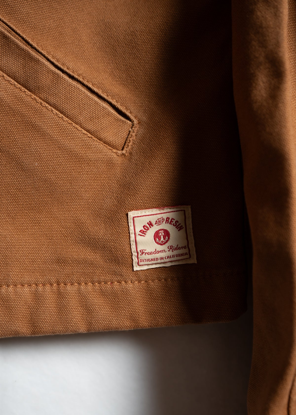 Close-up of a brown jacket with a pocket and an "Iron and Resin" label reading "Freedom Riders, Designed in California."