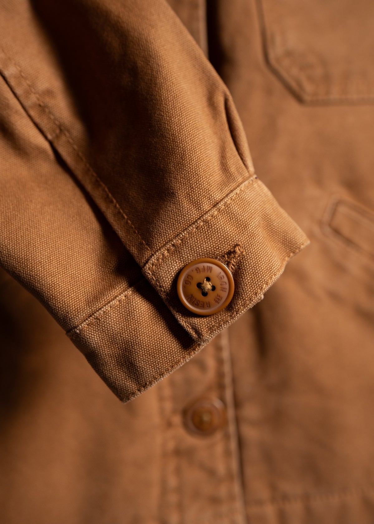 Close-up of a brown jacket sleeve with a button detail, showcasing textured fabric and stitching in warm lighting.