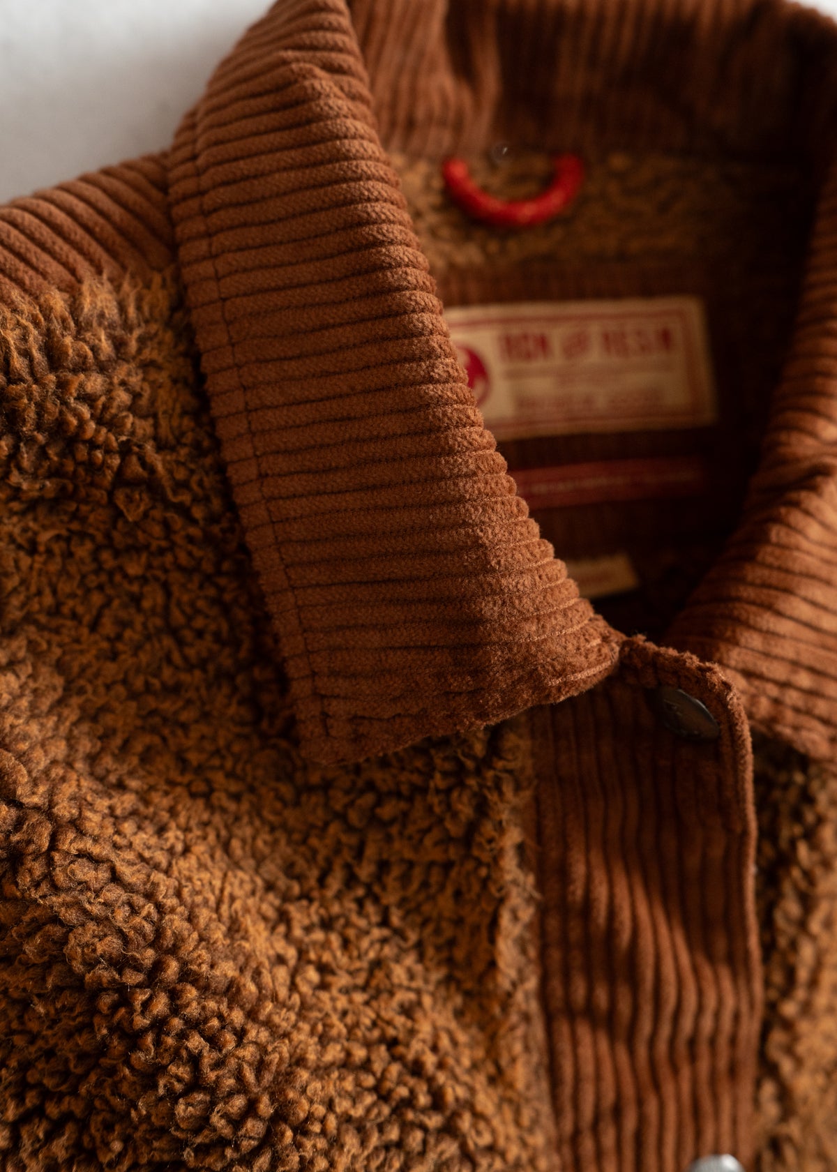 Close-up of a brown corduroy and shearling jacket collar with a visible label, highlighting texture and detail.