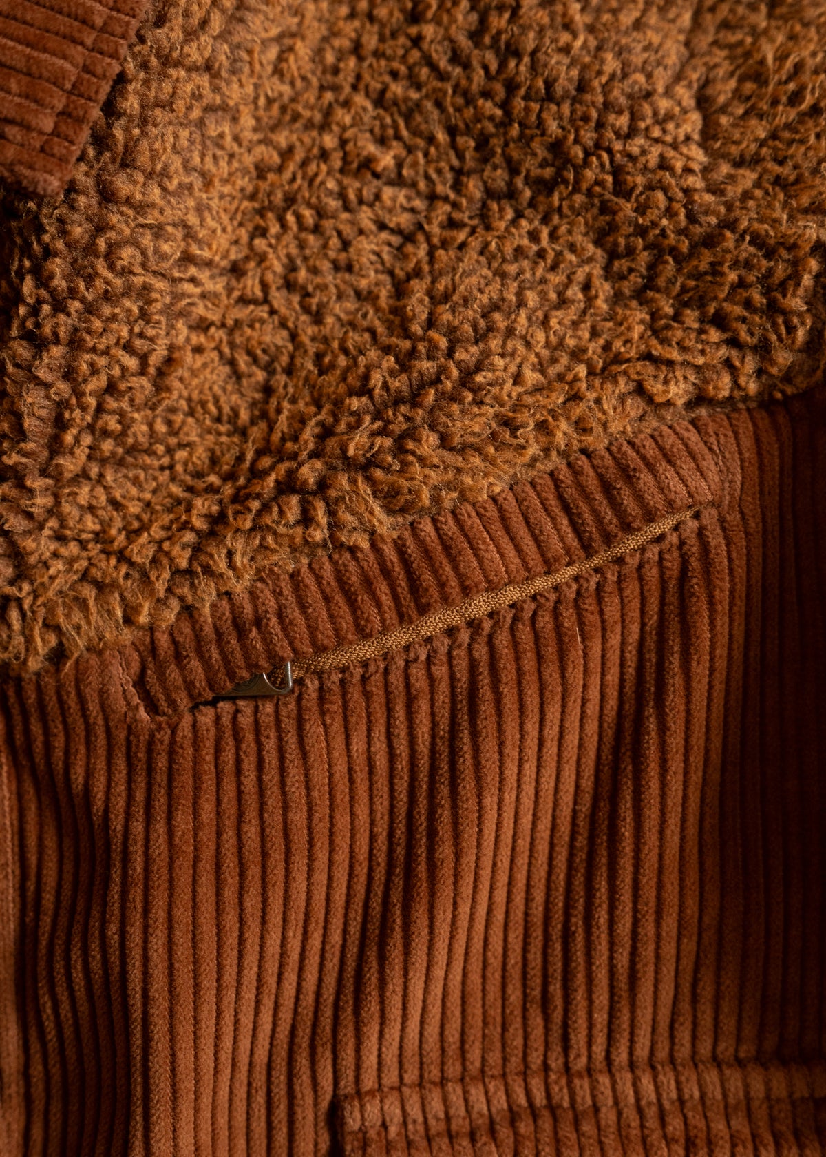 Close-up of brown corduroy fabric with a visible zipper, contrasted by a textured, fluffy material above.
