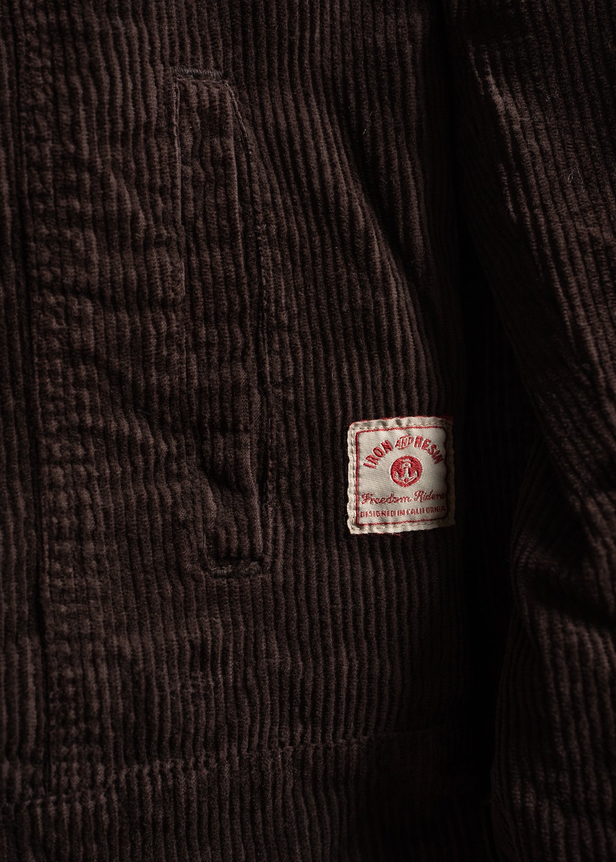 Close-up of a brown corduroy jacket with a visible pocket and an "Iron and Resin" label, highlighting texture and brand detail.