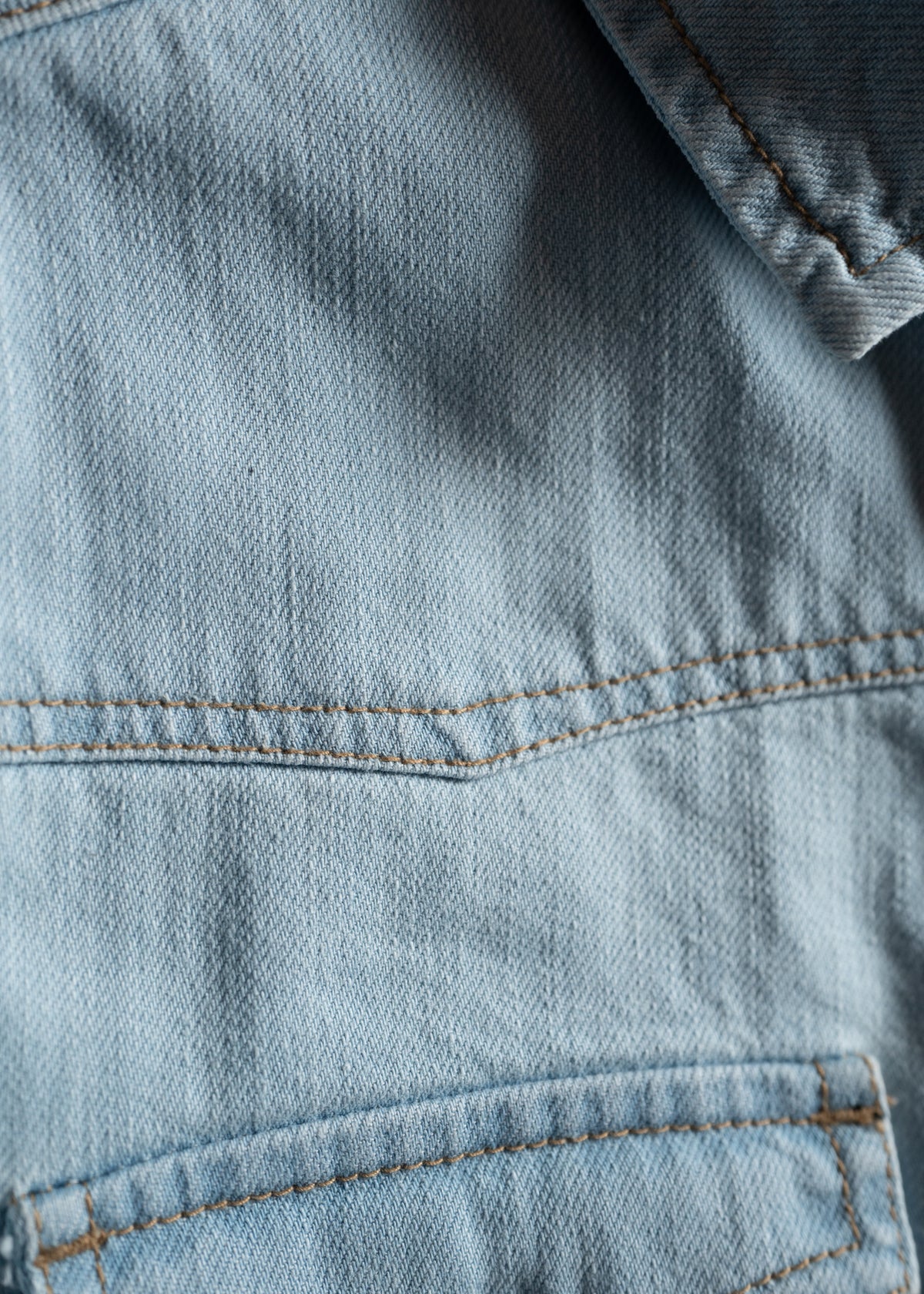 Close-up of light blue denim fabric with visible stitching and pocket detail, showcasing texture and craftsmanship.