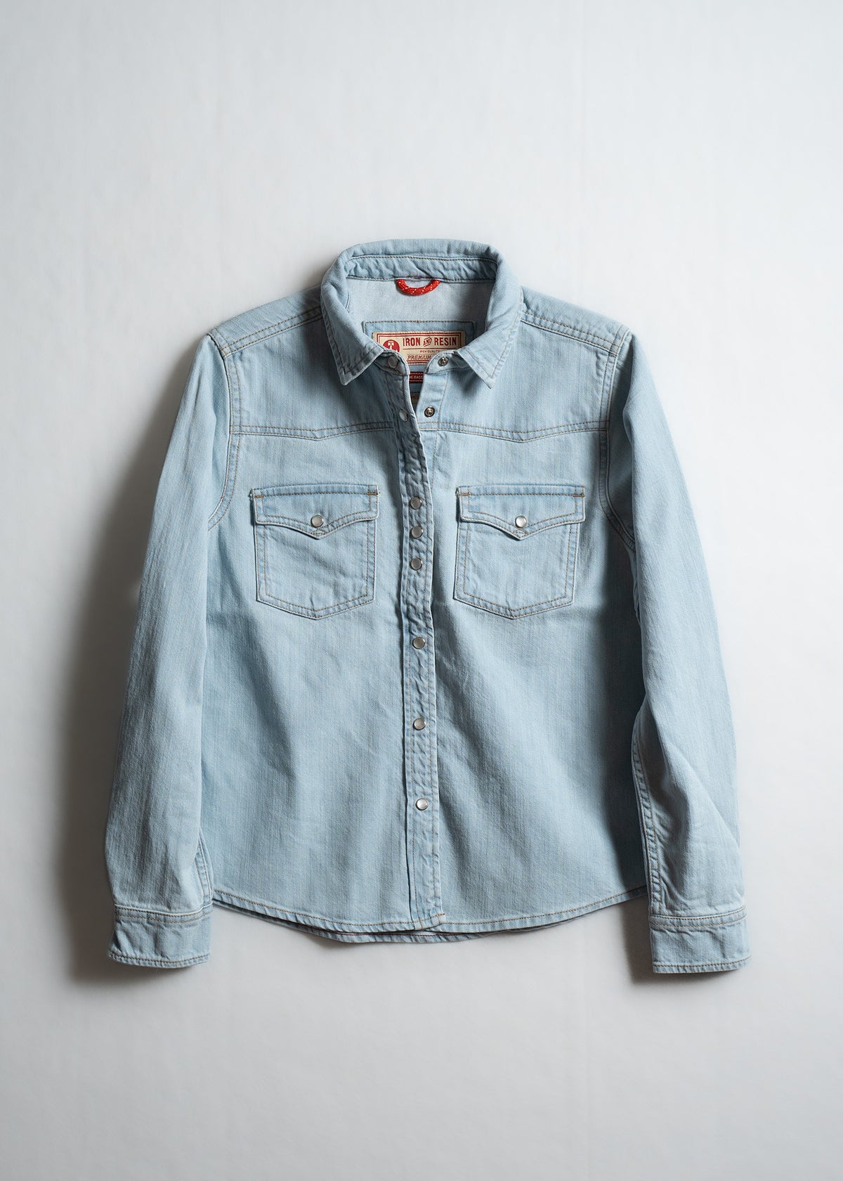 Light blue denim shirt with button-up front and two chest pockets, displayed against a plain white background.