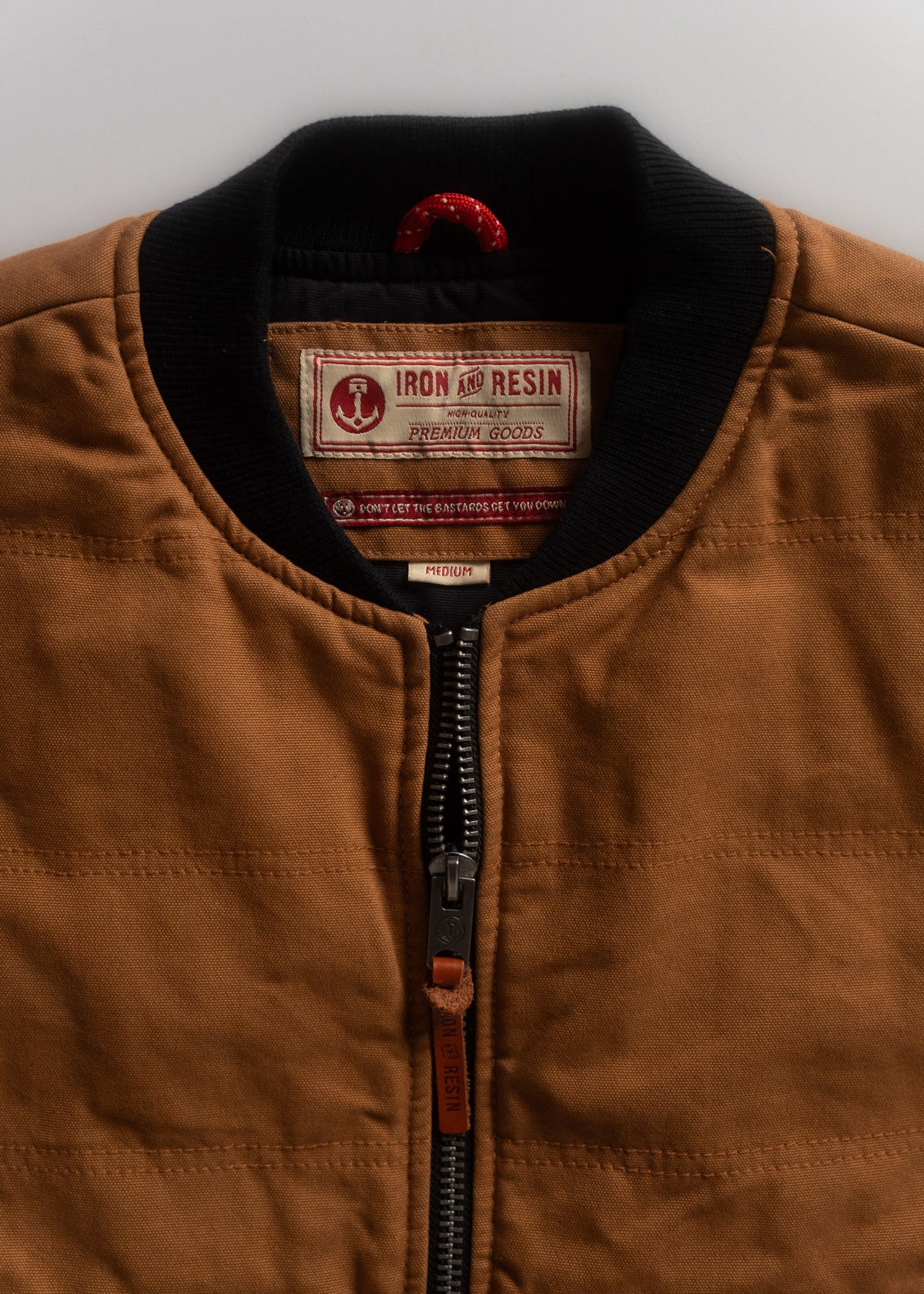 Brown jacket with black collar, featuring Iron and Resin label. Visible zipper and red hanging loop. Size medium.