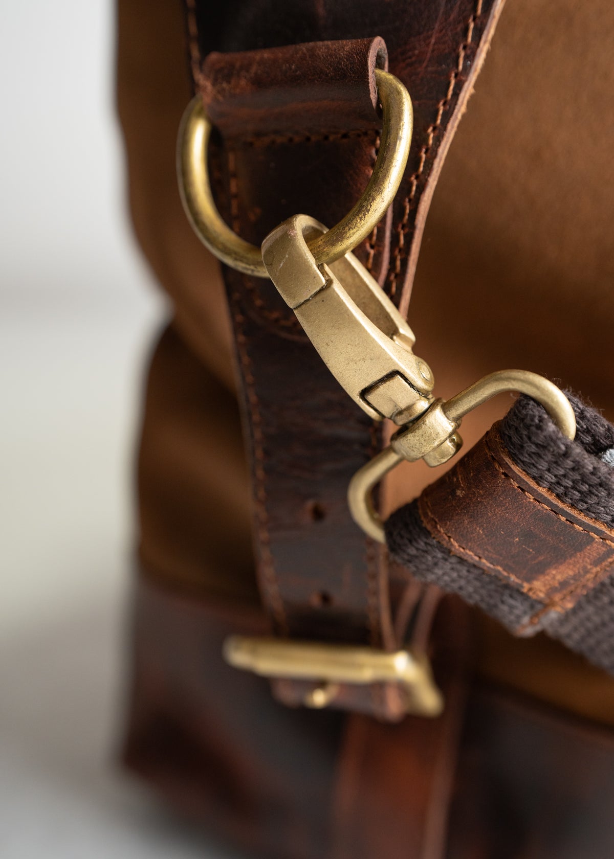 Close-up of a brown leather bag's brass buckle and strap, highlighting craftsmanship and durability in design.