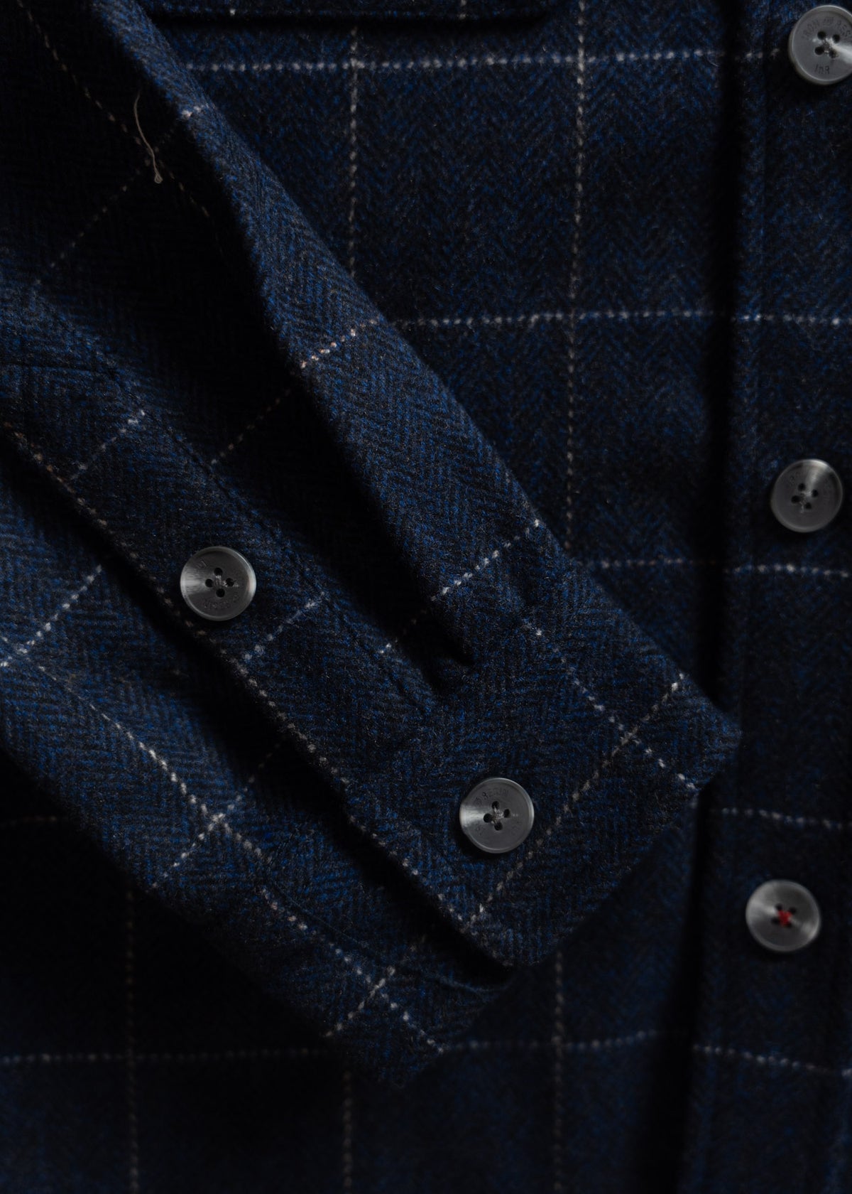 Close-up of a blue plaid wool shirt with buttoned cuff detail, showcasing a classic herringbone pattern and gray buttons.
