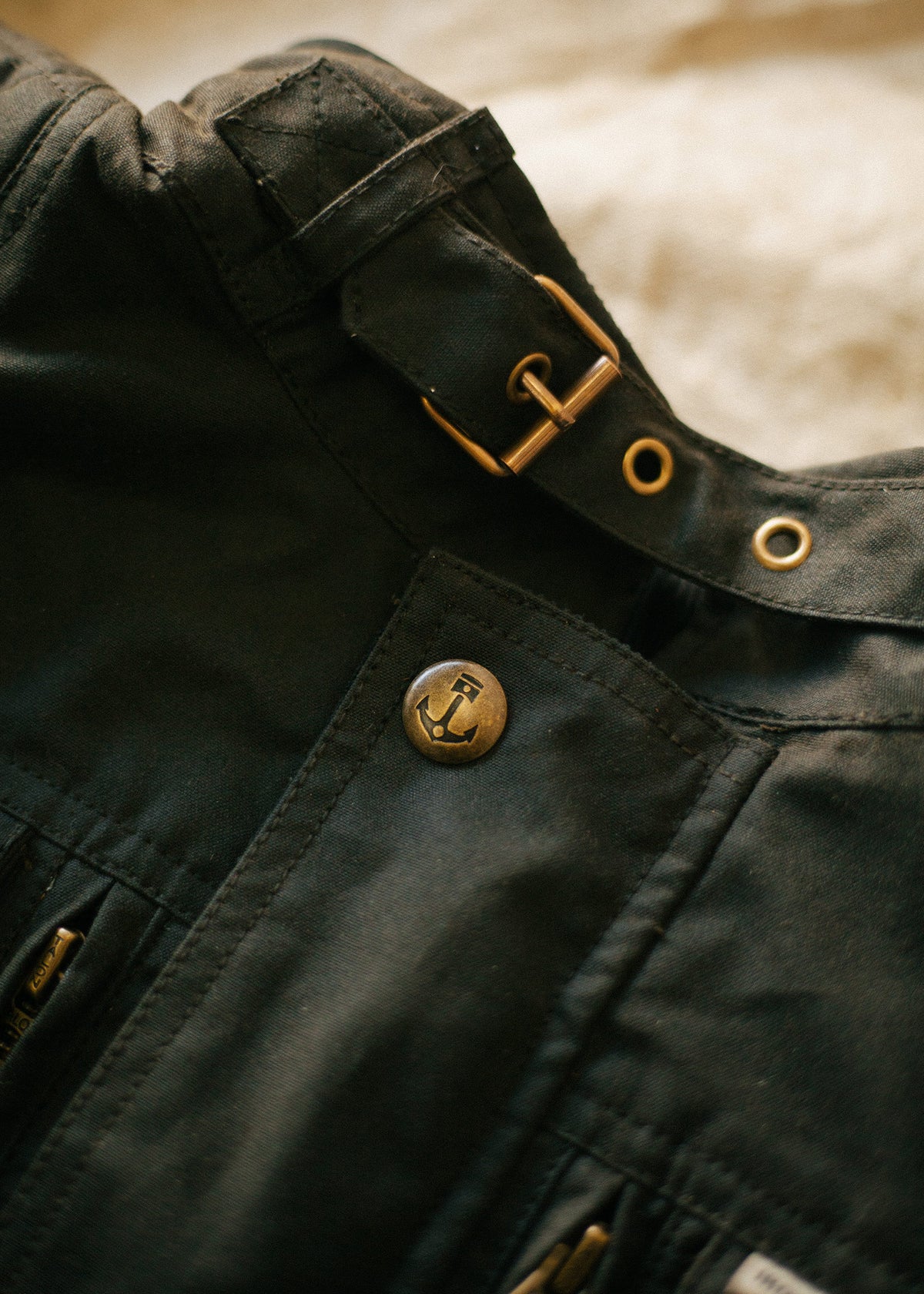 Close-up of a dark jacket featuring a brass anchor button and buckle, highlighting nautical style and detailed craftsmanship.