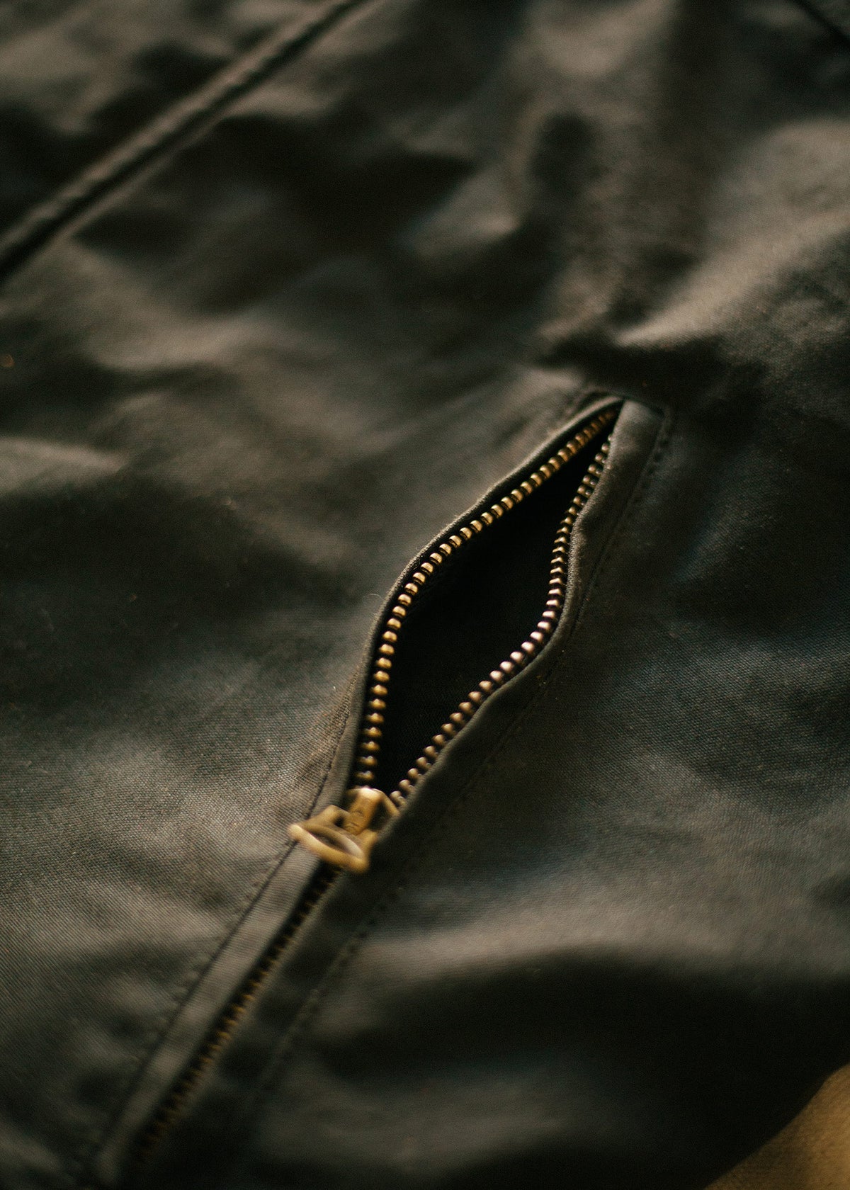 Close-up of a black jacket with a partially open zipper, highlighting the texture and detail of the fabric and metal teeth.