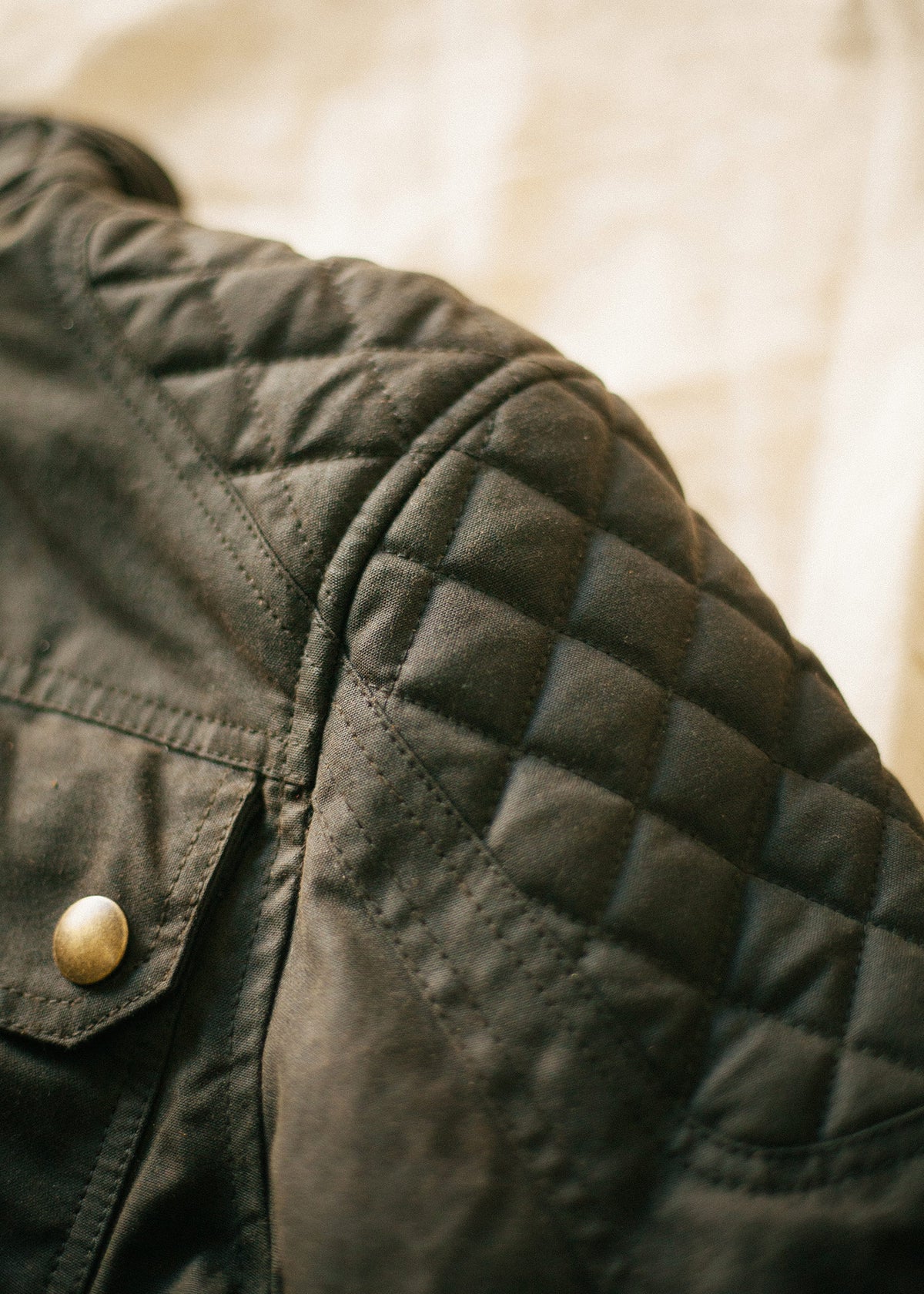 Close-up of a black quilted leather jacket shoulder with a brass button, highlighting texture and detail against a soft background.