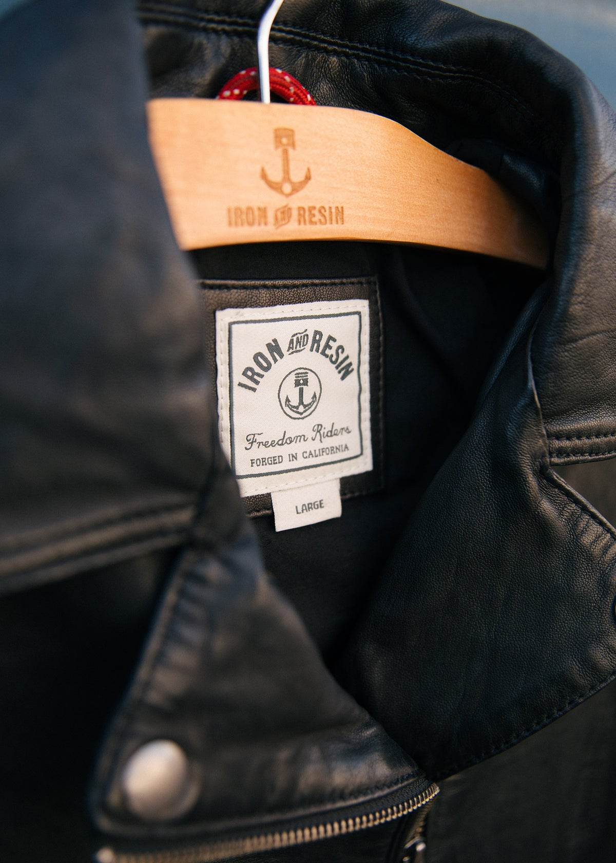 Close-up of a black leather jacket on a wooden hanger with "Iron and Resin" label, showcasing craftsmanship and style.