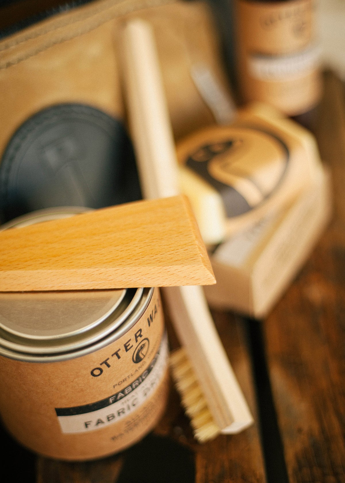 Wooden brush and fabric wax on a rustic table, with a leather pouch in the background, creating a vintage care kit vibe.
